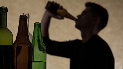 Bierflaschen im Vordergrund, im Hintergrund leicht unscharf ein männlicher Jugendlicher, der Bier trinkt