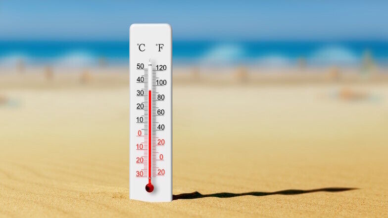 Thermometer steckt am Strand im Sand und zeigt auf etwa 34 Grad Celsius