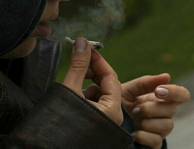 Junge Frau unter Kapuze raucht einen Joint, nur Mund und Hände sind zu sehen