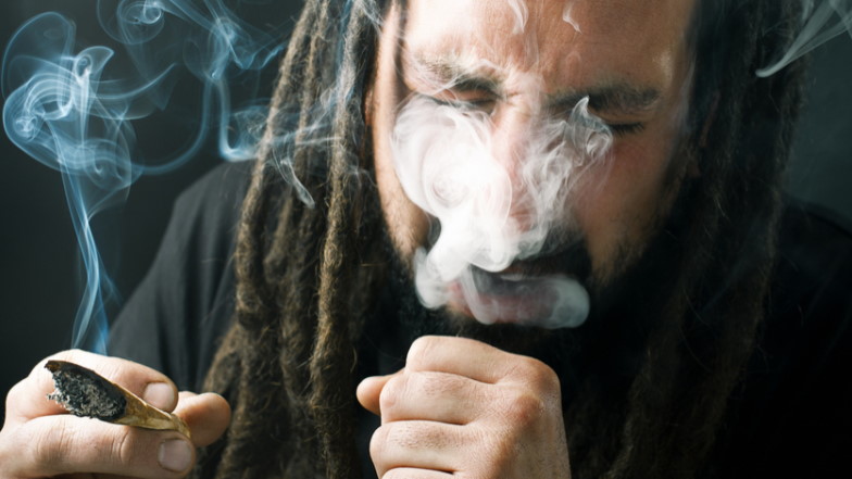 Männlicher Cannabiskonsument mit Joint atmet Rauch aus und hustet.