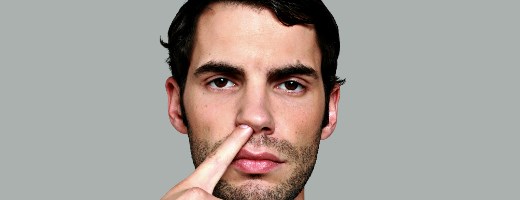 Mann steckt mit ausdrucksloser Mine Finger in die Nase