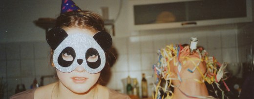 Junge Frau mit Pandamaske auf Party, im Hintergrund trinkt ein Jugendlicher Schnaps