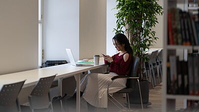 Studentin sitzt in einer Bibliothek mit dem Smartphone in der Hand