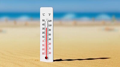 Thermometer steckt am Strand im Sand und zeigt auf etwa 34 Grad Celsius