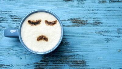 Kaffeebecher mit traurigem Gesicht auf Milchschaum