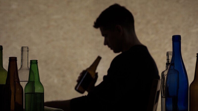 Von Flaschen umgebene Silhouette eines Manns, der eine Flasche in der Hand hältn der Hand