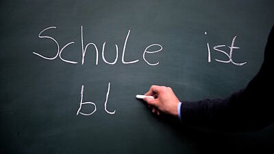 Jemand schreibt auf eine Tafel "Schule ist bl"