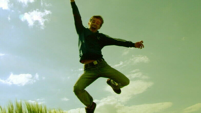 Junger Mann mit Trainingsjacke und Jeans springt vor Freude in die Luft