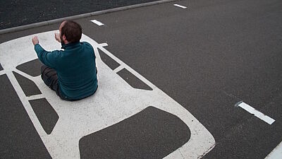 Mann sitzt in Fahrerposition auf aufgezeichnetem Auto auf dem Boden eines Parkplatzes