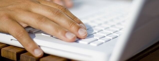 Hand auf der Tastatur eines weißen Notebooks