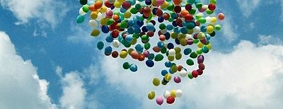 Eine Wolke von bunten Luftballons vor blauem Himmel und weißen Wolken