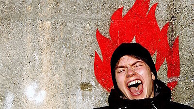 Jugendlicher steht vor gemalten Flammen vor einer Wand und schreit