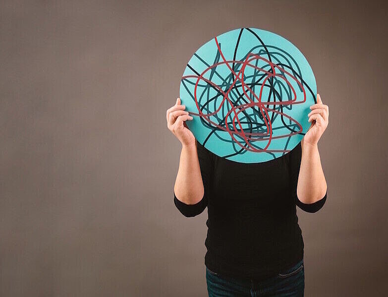 Mann hält rundes Schild mit wirren Linien drauf vor dem Kopf