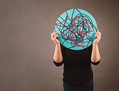 Mann hält rundes Schild mit wirren Linien drauf vor dem Kopf