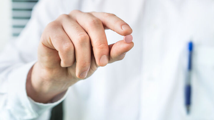 Mensch in weißem Kittel hält rote Pille zwischen Daumen und Zeigefinger