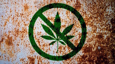 Grün durchgestrichenes Cannabisblatt im Stile eines Verbotsschilds auf rostigem Hintergrund