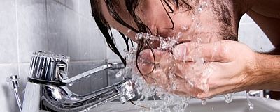Mann schüttet am Waschbecken Wasser ins Gesicht