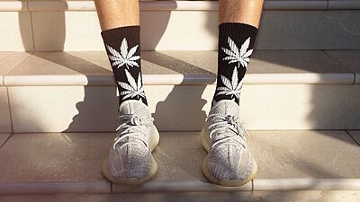 Nahhaufnahme von am Fuß getragenen Socken mit Cannabismotiven in Sportschuhen