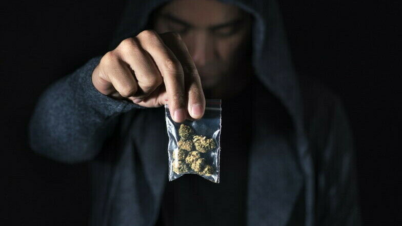 Mann im Hintergrund hält Plastiktütchen mit Cannabisblüten