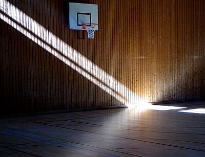 Basketballkorb in einer leeren Turnhalle; Sonnenstrahlen von links oben