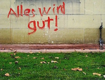 Grafittischriftzug "Alles wird gut" an einer Wand vor grünem Rasen