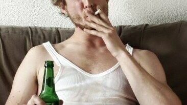 Mann auf Sofa kifft und hält Bierflasche in der Hand