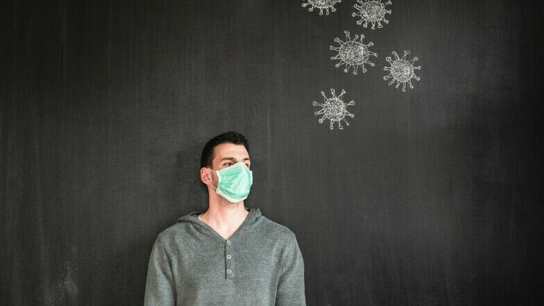 Mann mit Mund-Nasen-Schutz, im Hintergrund mit Kreide gemalte Coronaviren