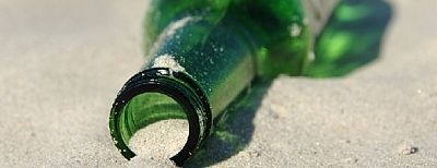Leere Bierflasche liegt im Sand, halb mit Sand gefüllt