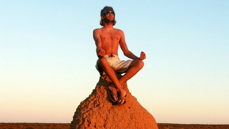 Mann mit freiem Oberkörper sitzt im Sonnenuntergang auf Termitenhügel und meditiert