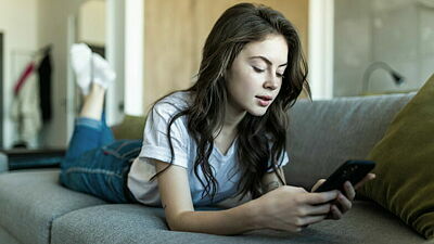 Jugendliche liegt auf dem Sofa und schaut auf ihr Smartphone