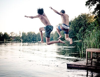 Zwei Jugendliche springen in einen Badesee