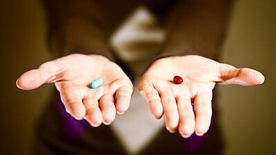 Frau hält blaue und rote Pille jeweils in ihren Händen