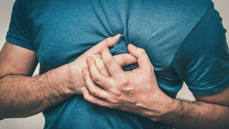 Mann in T-Shirt greift sich mit beiden Händen auf Herzhöhe an die Brust