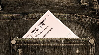 Eine ärztliche Krankschreibung steckt zum Teil in einer Jeansgesäßtasche