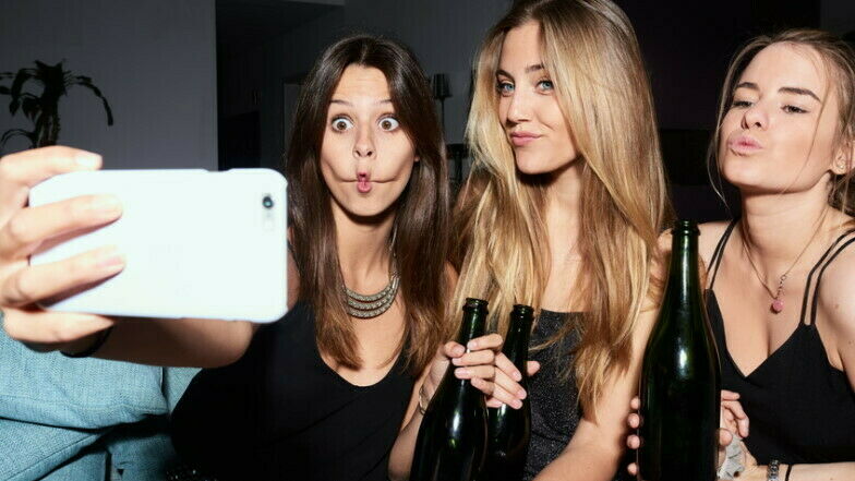 Drei junge Frauen machen Selfi mit Grimassen und Sektflasche in der Hand