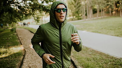 Mann in grüner Jacke und Kapuzze joggt durch einen Park