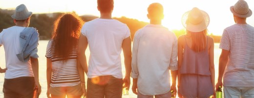 Männer und Frauen schauen in Sonnenuntergang mit Bierflaschen in der Hand