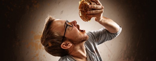 Mann isst mit weit aufgerissenem Mund einen Hamburger