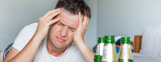 Mann hält sich schmerzverzerrt den Kopf, im Vordergrund leere Bierflaschen