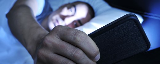 Mann liegt im Bett und schaut auf Smartphone in der Hand