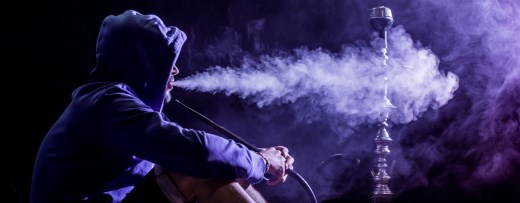 Mann mit Kapuzenpulli raucht Shisha vor dunklen Hintergrund