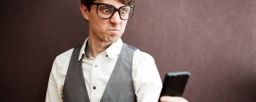 Mann mit Nerdbrille schaut wütend auf sein Smartphone