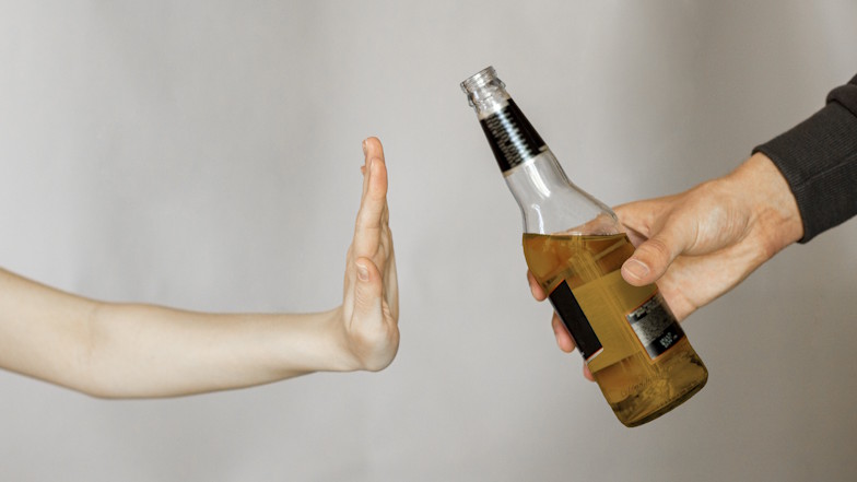 Weibliche Hand weist angebotene Bierflasche zurück