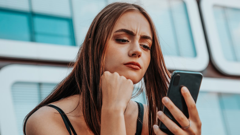 Junge Frau schaut stirnrunzelnd auf ihr Smartphone