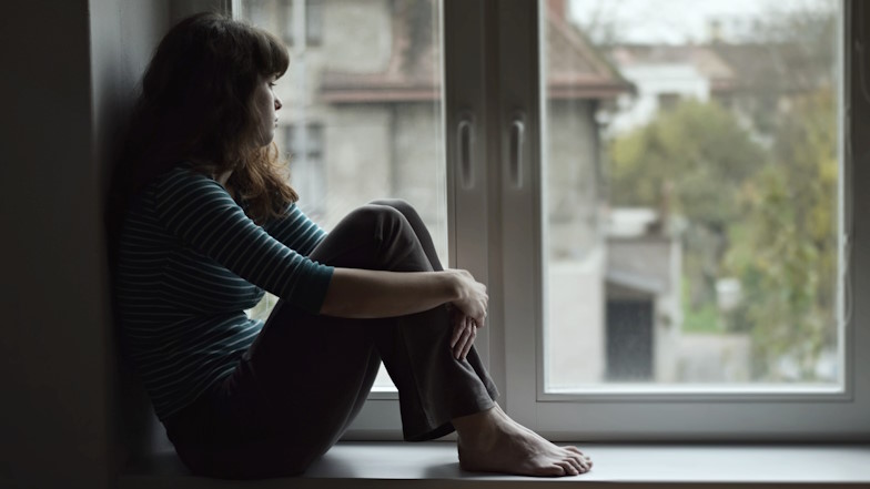 Jugendliche sitz am Fenster und schaut depressiv hinaus