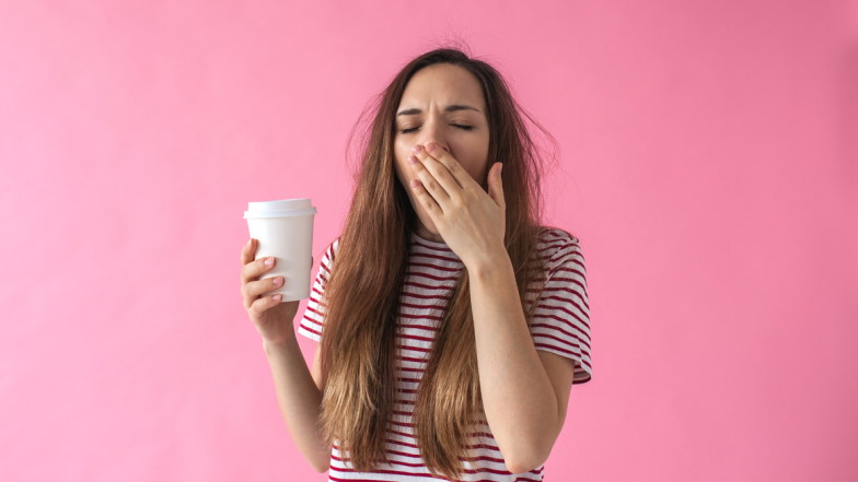 Junge Frau mit Kaffeebecher in der Hand gähnt