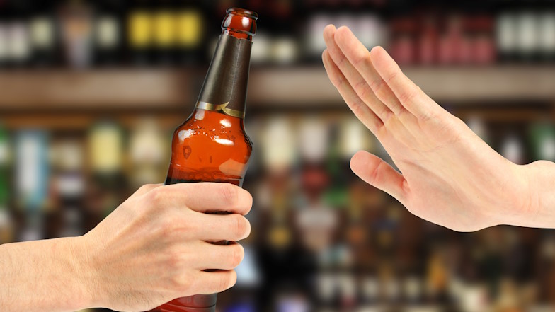 Jemand lehnt mit seiner Hand das Angebot einer Flasche Bier ab