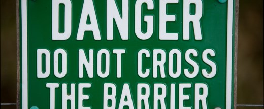 Grünes Schild mit Aufschrift "Danger do not cross the barrier"