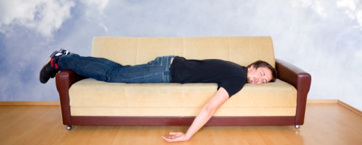 Junger Mann liegt der Länge nach auf dem Bauch und mit herabhängenden Armen auf einem Sofa.