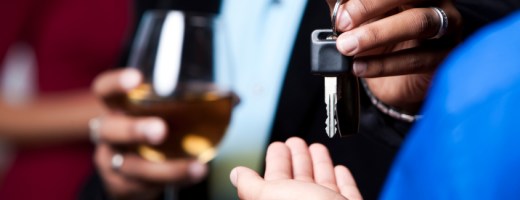 Person, die ein Glas Wein in der Hand hält, übergibt jemand anderem einen  Autoschlüssel